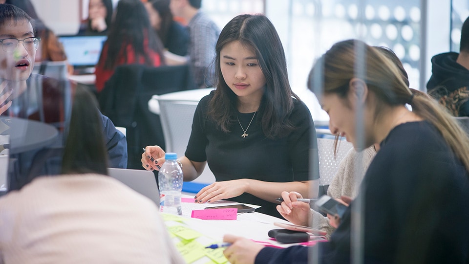 Students sitting down and working together around tables