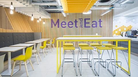 Tables and chairs in the cafeteria with a sign on the wall saying Meet and Eat.