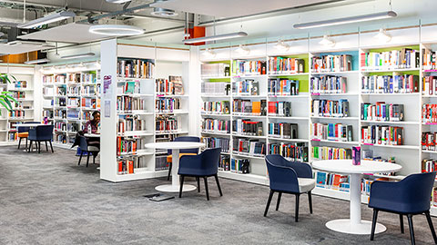 Library bookshelves filled with books and tables and chairs for students to work at.