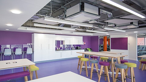 A Loughborough University London communal room with a kitchen, tables and stools/benches