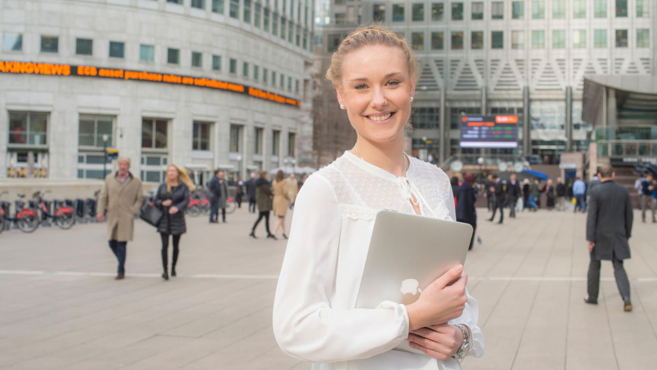 A student holding a laptop stood outside London office buildings