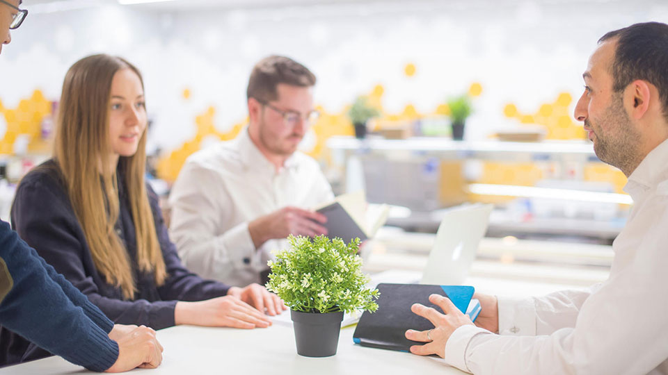 Three people sat around a table taking with notebooks and a plant on the table