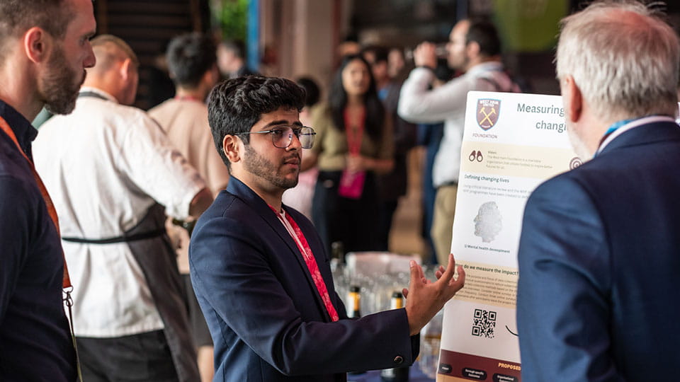 A student talking to a visitor in front of an exhibition board at the Collaborative Projects show