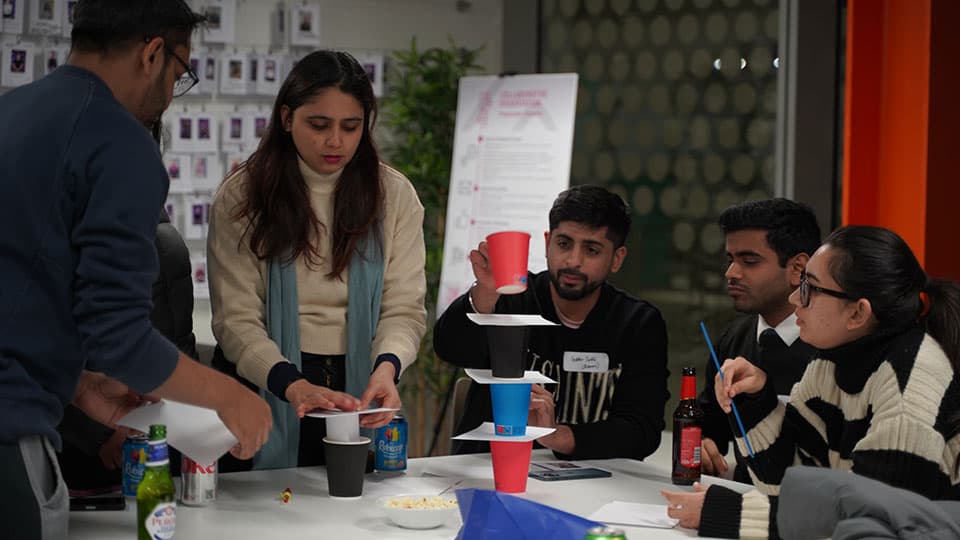 a group of students around tables working on a project using paper cups and paper