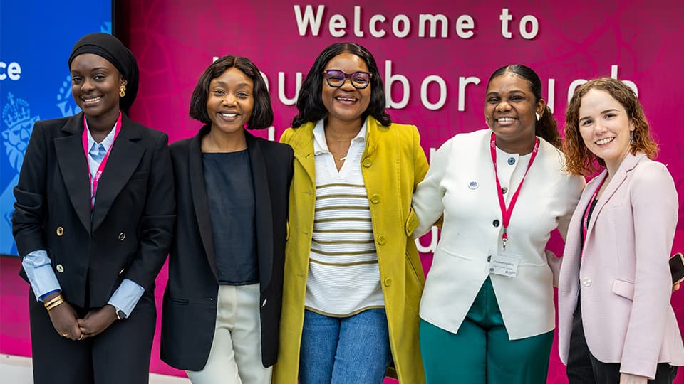 Group of students smiling at the camera in front of 'Welcome to Loughborough University London' sign