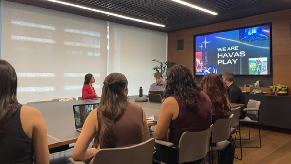 Students sitting in a meeting room looking at a screen which reads 'We are Havas Play'