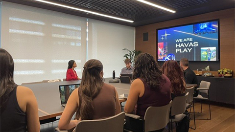 Students sitting in a meeting room looking at a screen which reads 'We are Havas Play'