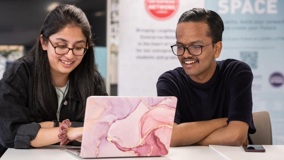 Two students sitting in front of a laptop smiling