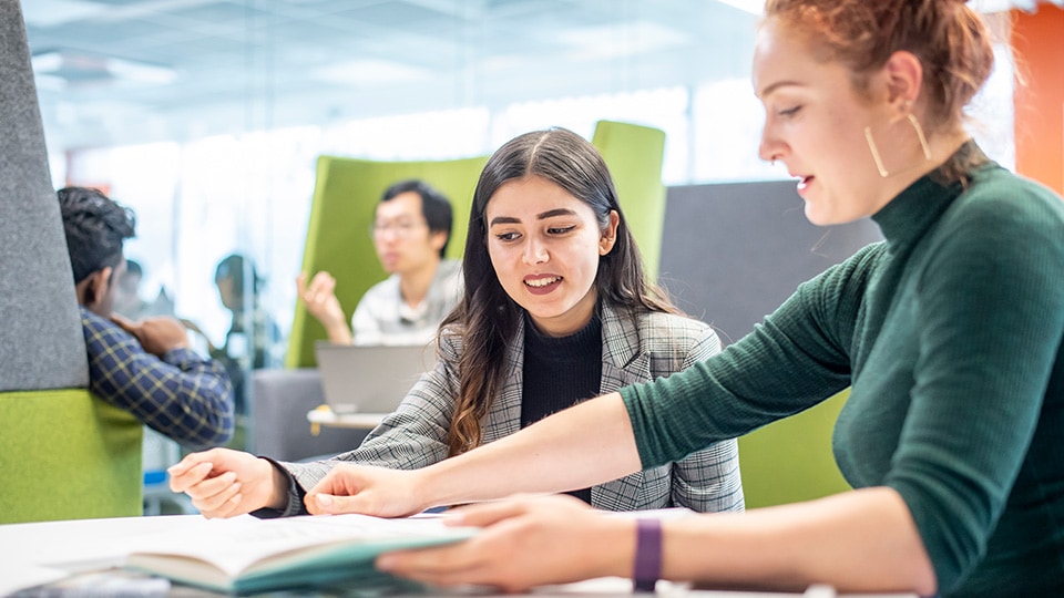 Two students are sitting down and looking through a study book together