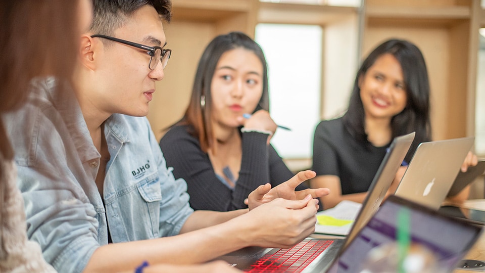 Four people are sitting down and working on their laptops together