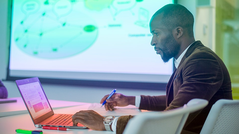 A person is sitting down and working on their laptop whilst writing notes
